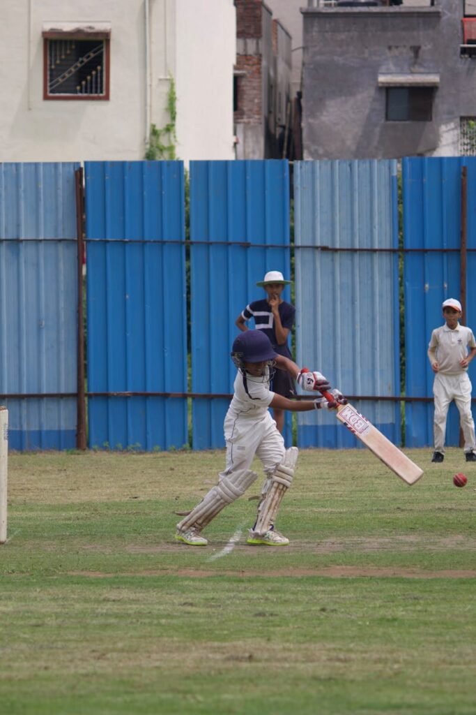 Action shot of teenagers playing cricket on a grassy field in Gahunje, India.