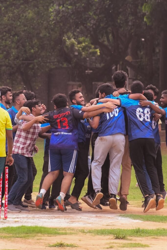 Excited group of male cricket players celebrate a win on a sports field outdoors.
